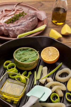 Onions, squid rings, green seaweed in frying pan. Squids on ceramic plate. top viewの写真素材