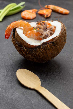 wooden spoon on table. Seafood cream soup in coconut. Shrimps and leeks. top view. black backgroundの写真素材