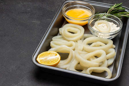Squid cut into rings in baking tray. Flour and beaten raw egg in bowls. top view. copyspace. black backgroundの写真素材