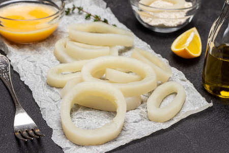 Squid cut into rings on paper. Fork and oil in bottle. Flour and beaten raw egg in bowls. top view. black backgroundの写真素材