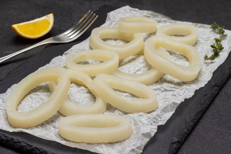 Squid cut into rings on stone board. Fork and lemon on table. top view. black background