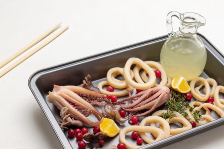 Seafood with lemon slices and bottle of lemon juice in baking tray. Bamboo sticks on table. top...