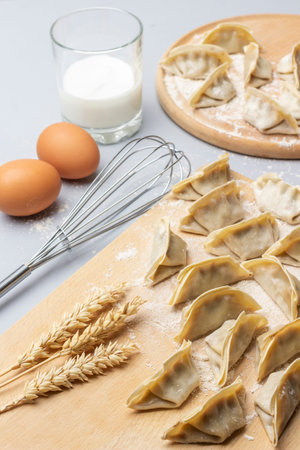 Raw gyoza dumplings on cutting board. Whisk, two eggs and glass of milk. top view. gray background.