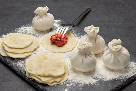 Meat filling with fork on piece of dough. Raw dumplings, pieces of dough and flour on stone black board. top view. black backgroundの写真素材
