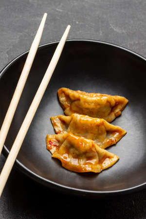Chopsticks and three gyoza dumplings in black bowl. close-up. black backgroundの写真素材