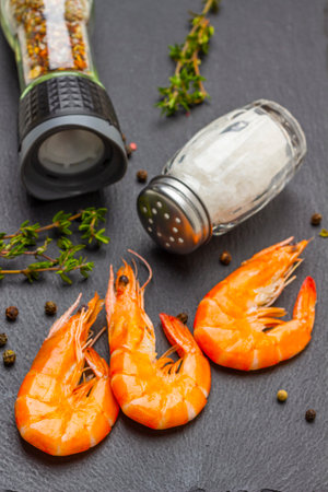 Shrimps, salt in glass jar, spices and thyme sprigs on black. flat layの写真素材