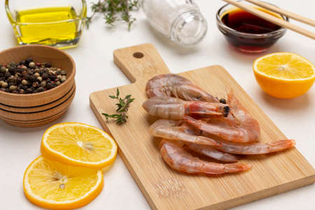 Raw shrimp on cutting board. Lemon slices, allspice in bowl, soy sauce on table. top view. white backgroundの写真素材