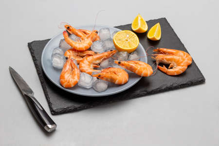 Shrimps, lemon and ice on a gray plate and on a stone surface. Knife on the table. top view. gray backgroundの写真素材