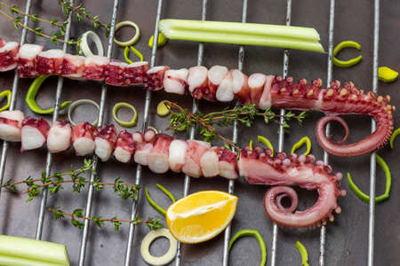 Octopus tentacles on the grill. Thyme sprigs, lemon and celery stalk. flat lay. rusty metal backgroundの写真素材