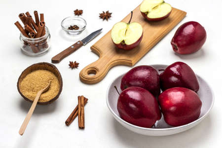 Ripe red apples in a bowl. Brown sugar in coconut shell. Cinnamon sticks in glass jar. Apple halves on cutting board. top view. white backgroundの写真素材