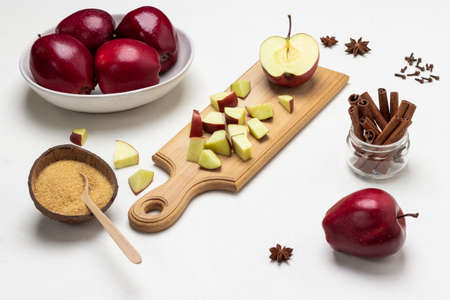 Chopped apples on cutting board. Brown sugar in coconut shell. Cinnamon sticks in glass jar. Ripe red apples in a bowl. top view. white backgroundの写真素材