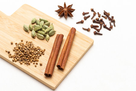 Coriander seeds, cinnamon sticks, and cardamom on wooden board. Cloves and star anise on table. top view. white backgroundの写真素材