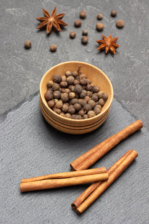 Allspice in wooden bowl and cinnamon sticks on stone board. Star anise and allspice on the table. top view. black backgroundの写真素材