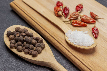 Allspice in wooden spoon. Pods of red pepper and salt blackboard. close up. black backgroundの写真素材