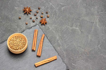 Coriander seeds in wooden bowl and cinnamon sticks on stone board. Star anise and allspice on table. copyspace. top view. black backgroundの写真素材