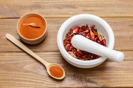 Dry red pepper pods in porcelain mortar. Ground red pepper in wooden bowl. flat lay. wooden backgroundの写真素材