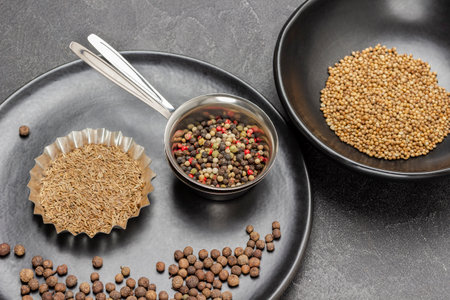 Allspice and cumin seeds in metal bowls on black plate. Coriander seeds in black bowl. top view. black backgroundの写真素材