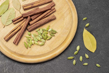 Cardamom, bay leaf and cinnamon sticks on board. flat lay. black backgroundの写真素材
