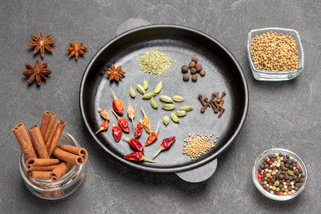 Cinnamon sticks, red pepper pods, star anise and cloves in frying pan. flat lay. black backgroundの写真素材