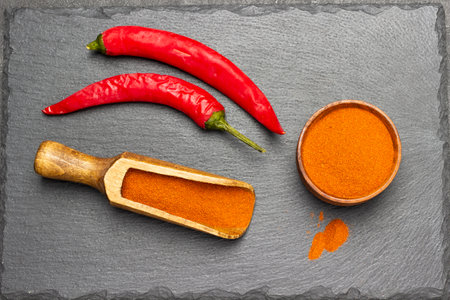 Fresh red pepper on stone board. Ground paprika in bowl and scoop. flat lay. black backgroundの写真素材
