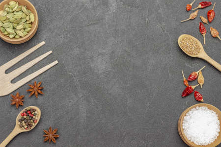 Salt and cardamom in bowls, allspice and mustard seeds in wooden spoons, dry red pepper pods, star anise and wooden fork around the edges of picture. copyspace. flat lay. black backgroundの写真素材