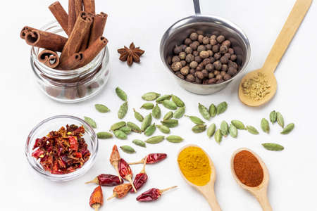 Allspice in metal bowl and cinnamon sticks in jar. Ground spices paprika, turmeric and ginger. Cardamom seeds and dry red pepper pods. top view. white backgroundの写真素材