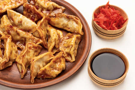 Boiled gedza dumplings in sauce on ceramic plate. Pickled ginger and soy sauce in bowls. top view. white backgroundの写真素材