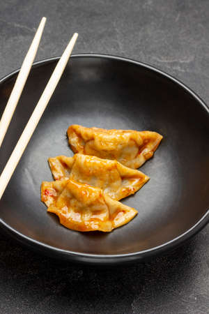 Chopsticks and three gyoza dumplings on black bowl. top view. black backgroundの写真素材