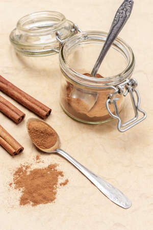 Ground cinnamon in metal spoon and on table. Ground cinnamon and spoon in glass jar. top view. brown background.の写真素材