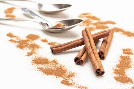 Cinnamon sticks among ground cinnamon, metal spoons on table. close up. top view. white backgroundの写真素材