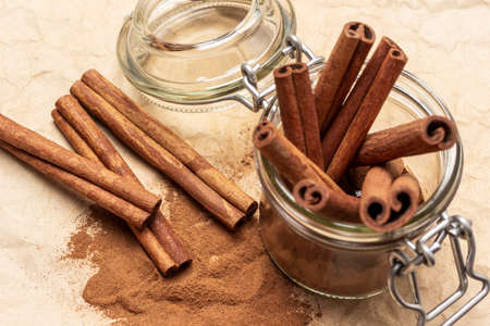 Cinnamon sticks in glass jar. Cinnamon sticks and ground cinnamon and on table. flat lay. brown background.の写真素材
