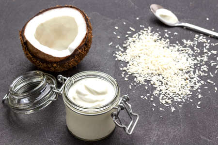 Half coconut and glass jar of coconut yogurt. Coconut flakes on table. Black background. top viewの写真素材