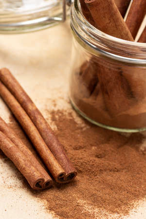 Cinnamon sticks and ground cinnamon and on table. Cinnamon sticks in glass jar. close up. brown background.の写真素材