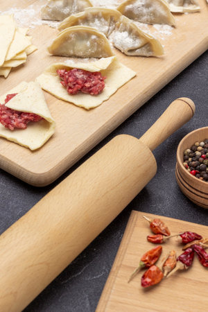 Rolling pin, allspice and pepper pods on table. Minced meat on piece of dough and raw gyoza dumplings on board. top view. black backgroundの写真素材