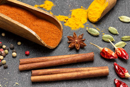 Ground paprika and turmeric in wooden scoop. Cinnamon sticks and spices on table. top view. black backgroundの写真素材