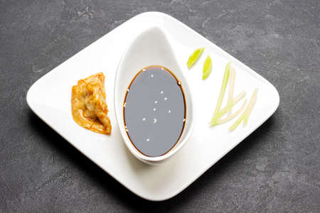 Boiled gyoza dumpling and chopped leek on white plate. Soy sauce in porcelain bowl. top view. black backgroundの写真素材