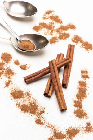 Cinnamon sticks among ground cinnamon, metal spoons on table. close up. top view. white backgroundの写真素材