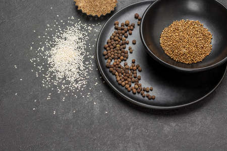 Allspice on black porcelain plate. Coriander seeds in black bowl. Sesame seeds on table. copyspace. top view. black backgroundの写真素材