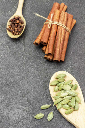 Cardamom in wooden spoon, bunch of cinnamon sticks and cloves in spoon. copyspace. top view. black backgroundの写真素材