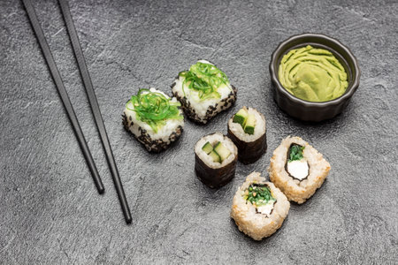 Sushi set with seaweed, black sesame and cucumber. Chopsticks, wasabi in black bowl. top view. black backgroundの写真素材
