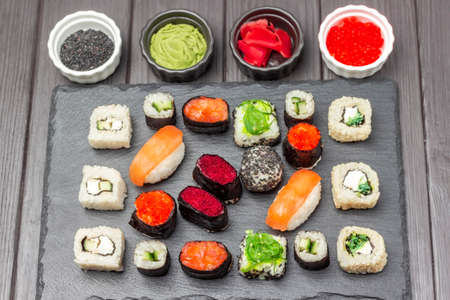 Sushi set on black stone board. Wasabi, pink ginger, black sesame in bowls. top view. dark wooden backgroundの写真素材
