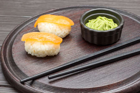Sushi with salmon, black chopsticks and wasabi on cutting board. Dark wooden background. top viewの写真素材