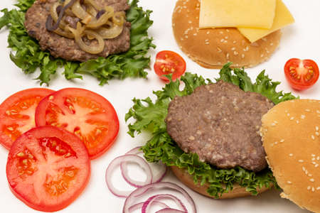 Fried burger bun on lettuce leaf, fried burger with cheese and fried onions, chopped tomatoes and onions. flat lay. white backgroundの写真素材
