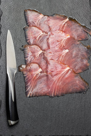 Kitchen knife and thin slices of tuna on stone board. flat lay. dark background.の写真素材