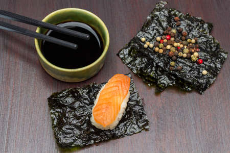 Sushi with salmon on nori sheet. Allspice on nori sheet. Soy sauce and chopsticks in a bowl. top view. brown background.の写真素材