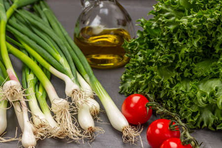 Green onions with roots, lettuce, tomatoes and a bottle of olive oil. gray background. top viewの写真素材