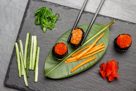 Sushi and sliced carrots on green leaf. Sliced cucumbers and seaweed on stone board. flat lay. gray backgroundの写真素材