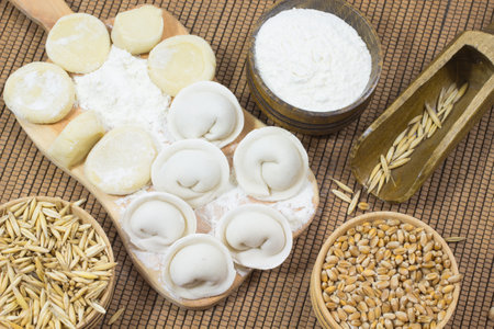 Raw dumplings on the board. Wheat in the box. Grains of oats in a spoon and a box. Flour in a Boxの写真素材