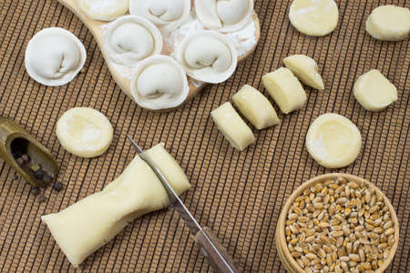 Dumplings on the board, cutting the dough into pieces, the knife, the wheat grain in the box, spices in a wooden spoonの写真素材