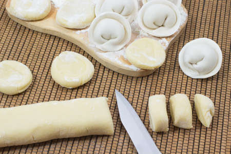 The cut pieces of dough. Knife. Uncooked dumplings on the board. Flourの写真素材